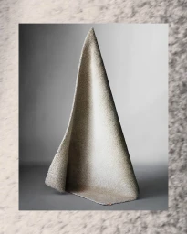 A sculptural grey textured textile piece draped in a tall conical form on a gradient studio floor with a framed border.