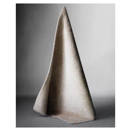 A rolled textured beige fabric or rug standing vertically in a cone shape on a grey studio floor.