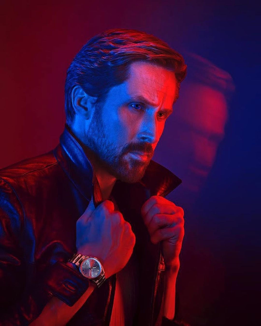 Portrait of a man with short brown hair, wearing a leather jacket and a wristwatch, with red and blue lighting effects.