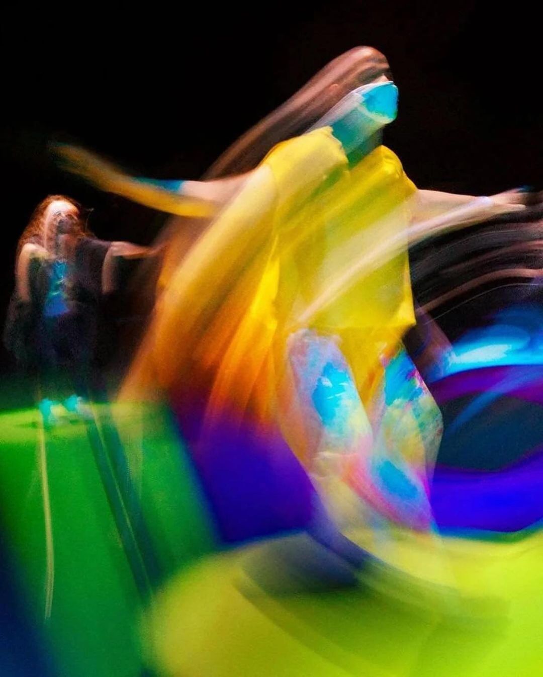 Two figures blurred in motion, one in yellow facing right, the other in black facing left, against a gradient floor and black background.