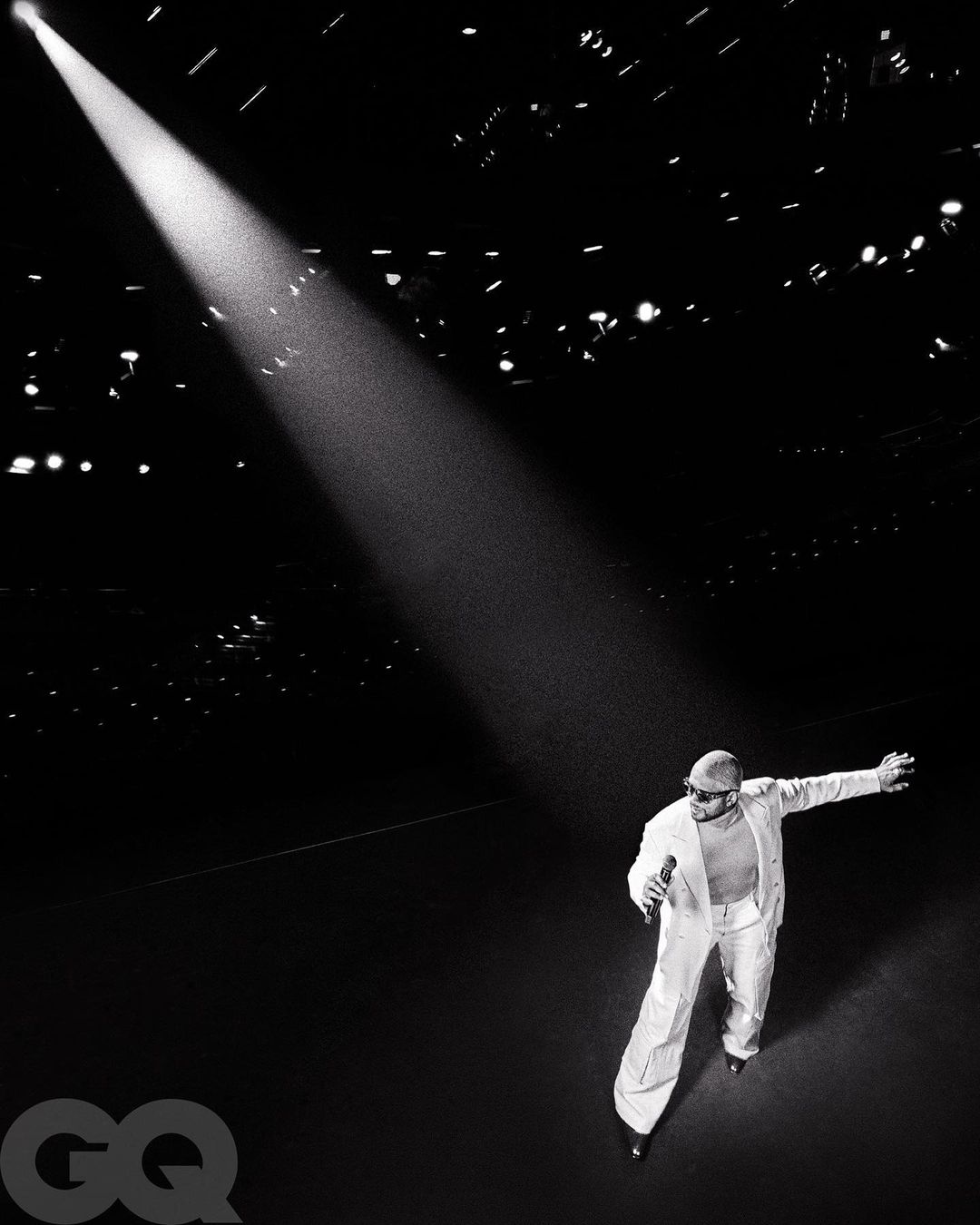 A singer in white suit under a spotlight sings on a dark stage, creating a dramatic monochrome image for music or entertainment use.