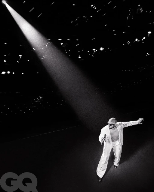 A singer in white suit under a spotlight sings on a dark stage, creating a dramatic monochrome image for music or entertainment use.