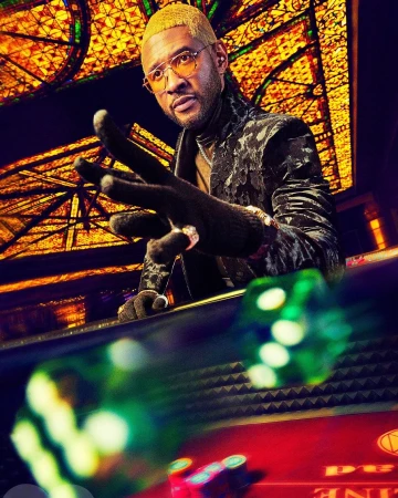 Usher poses near dice table at casino. He's wearing gloves, gold-rimmed glasses, and a black patterned velvet jacket in a low-angle shot.