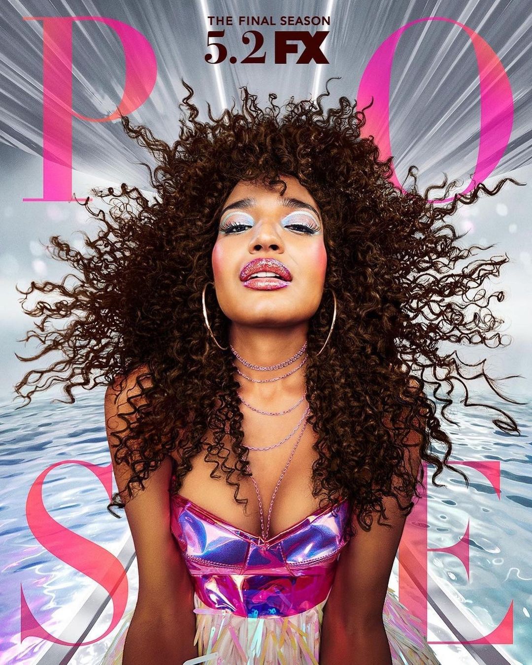 Promotional close-up of an adult woman with brown curly hair and iridescent bodice, against a reflective silvery background.