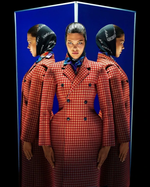 Fashion shot of an adult woman in red houndstooth coat with a black patterned scarf, posed against a blue studio background.