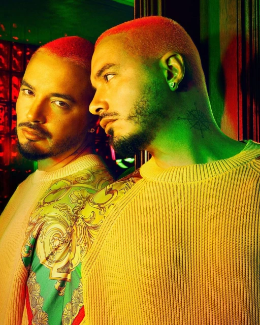 Portrait of a stylish adult male with orange hair, a beard, and a patterned yellow sweater, reflected in a mirror with green and red lighting.