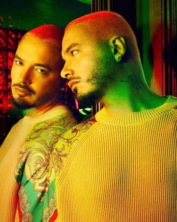 Portrait of a stylish adult male with orange hair, a beard, and a patterned yellow sweater, reflected in a mirror with green and red lighting.