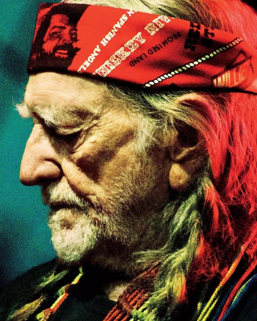 Close-up profile portrait of an elderly man with a red bandana, long white hair and beard, and a multicolored scarf.