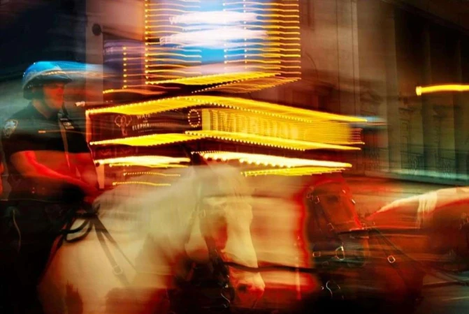 Motion blur image of a mounted police officer and a horse in an urban setting with bright yellow lights and a sign in the background.