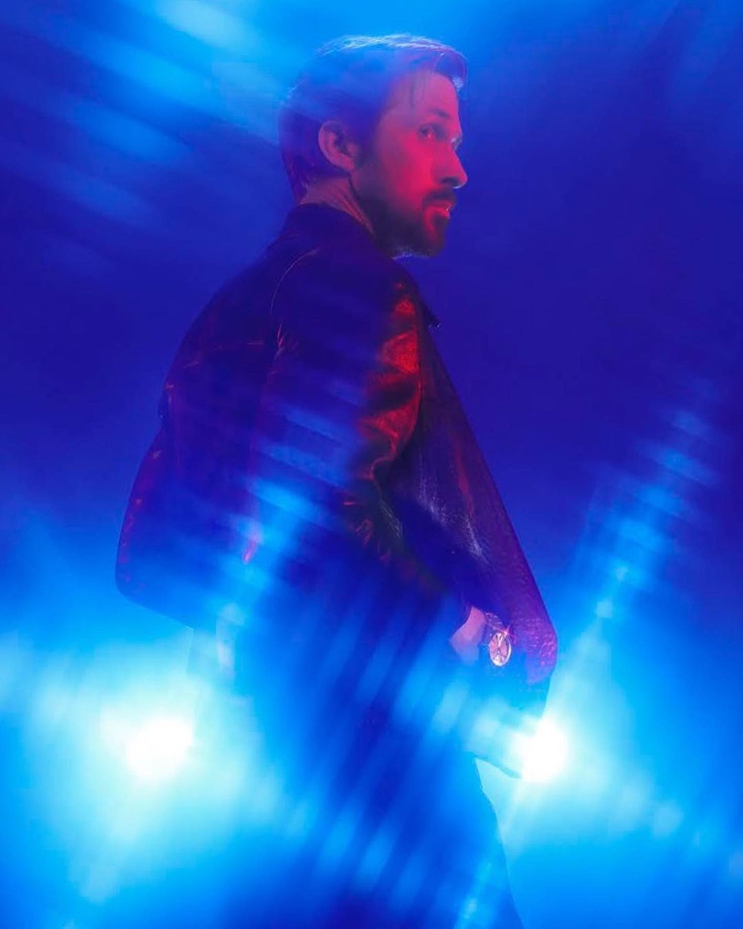Profile shot of a bearded adult male wearing a dark leather jacket against an abstract blue background with artistic lighting effects.