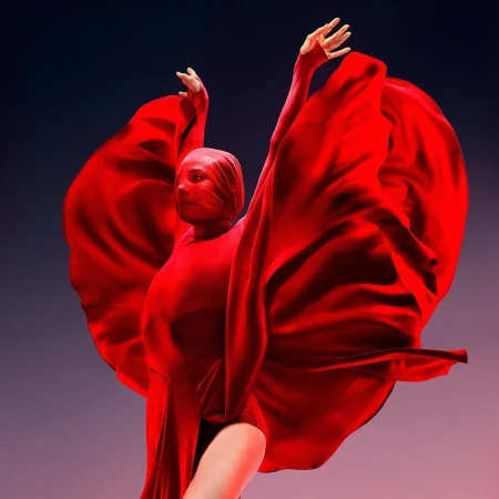 Dancer in a vivid red costume with large flowing fabric wings raised against a dark gradient background.