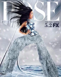 Woman in mirrored mosaic top and silver fringe pants posing dramatically with long dark hair blowing in the wind.