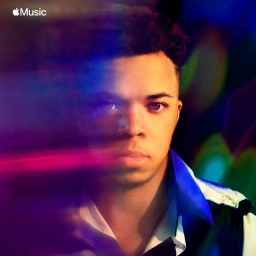Portrait of a Black man with short dark hair wearing a collared shirt, set against a motion-blurred colorful abstract background.