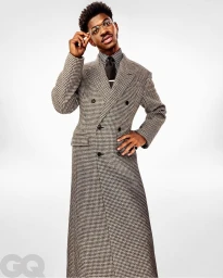 Lil Nas X wearing a houndstooth double-breasted coat and glasses against a white background by Pari Dukovic