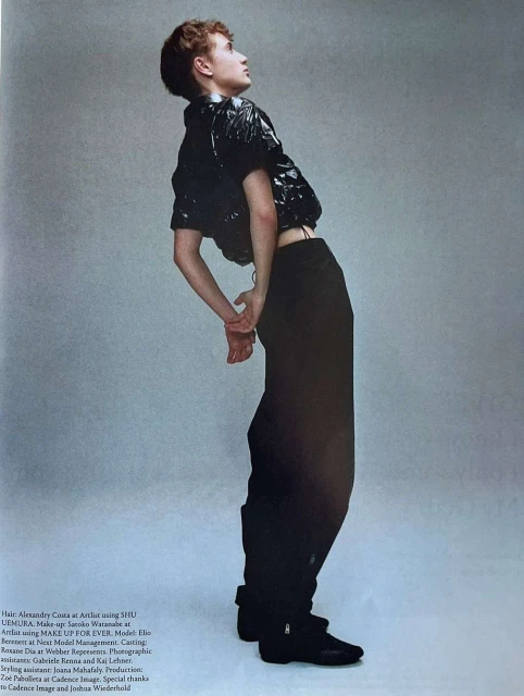 Fashion editorial shot of a young adult female fashion model posing in a studio wearing a black vinyl jacket and wide-leg pants.