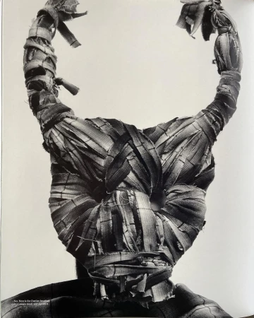 Monochrome image of a mask-like head covering made of woven material, featuring prominent curved horns, set against a light background.