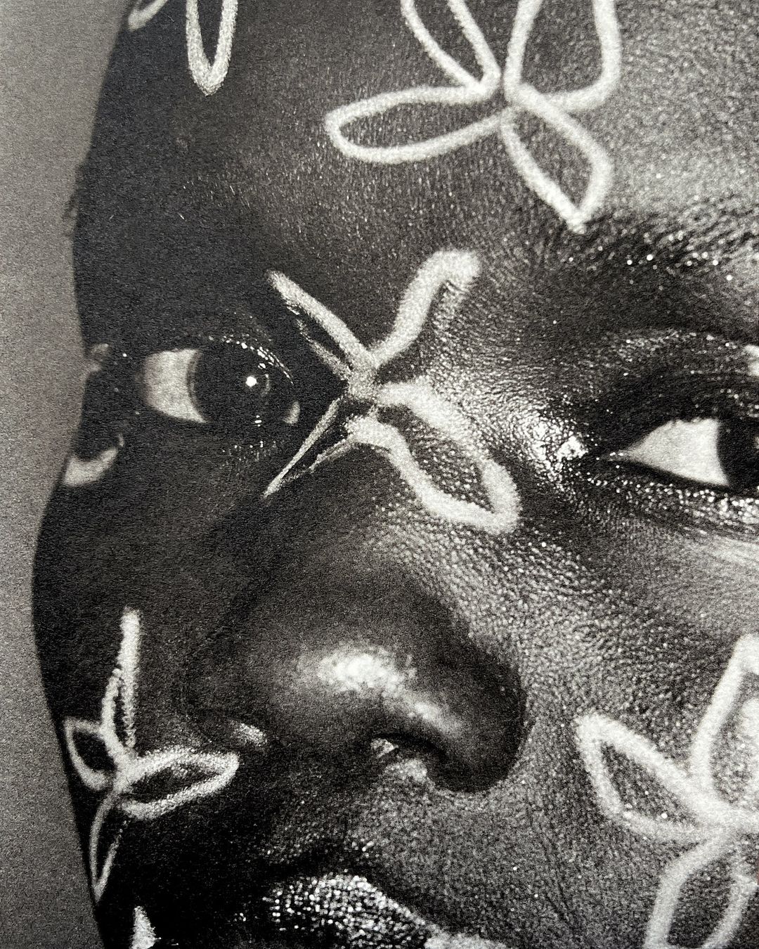 Close-up portrait of a Black woman with floral face paint, emphasizing beauty and artistic expression in a high-contrast, black-and-white image.