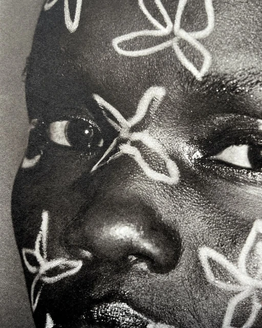 Close-up portrait of a Black woman with floral face paint, emphasizing beauty and artistic expression in a high-contrast, black-and-white image.