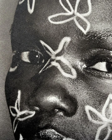 Close-up portrait of a Black woman with floral face paint, emphasizing beauty and artistic expression in a high-contrast, black-and-white image.