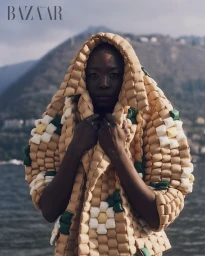Model in quilted beige hooded jacket with flower pattern by water and mountains