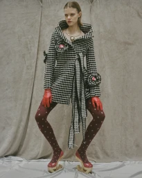 Model wearing a black and white patterned coat, red leather gloves, and polka dot tights with carved wooden platform shoes.