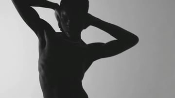 Striking black and white studio shot of a shirtless adult male with arms raised, showcasing athletic physique and silhouette against a light backdrop.