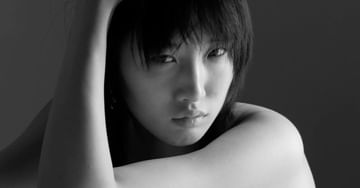 Close-up black and white portrait of a young adult woman with short dark hair, eyes open, and arm raised in a photo studio.