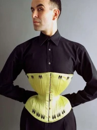 Man wearing a black shirt and a structured yellow-green corset against a plain grey background