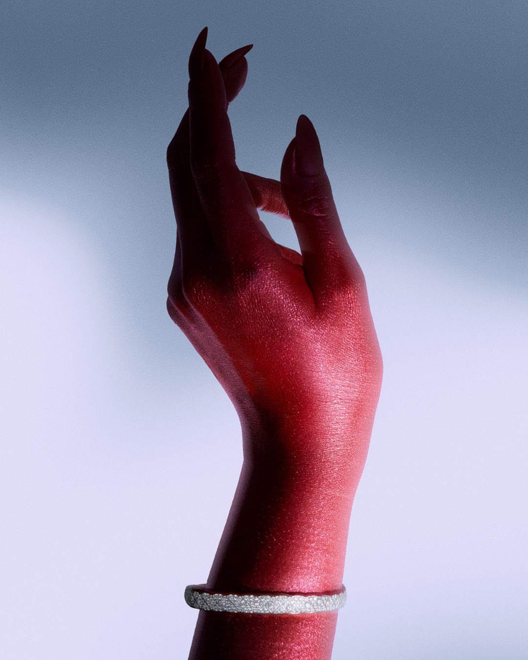 Close-up studio shot of a raised adult hand with red body paint, wearing a white rhinestone bracelet, against a gradient background.