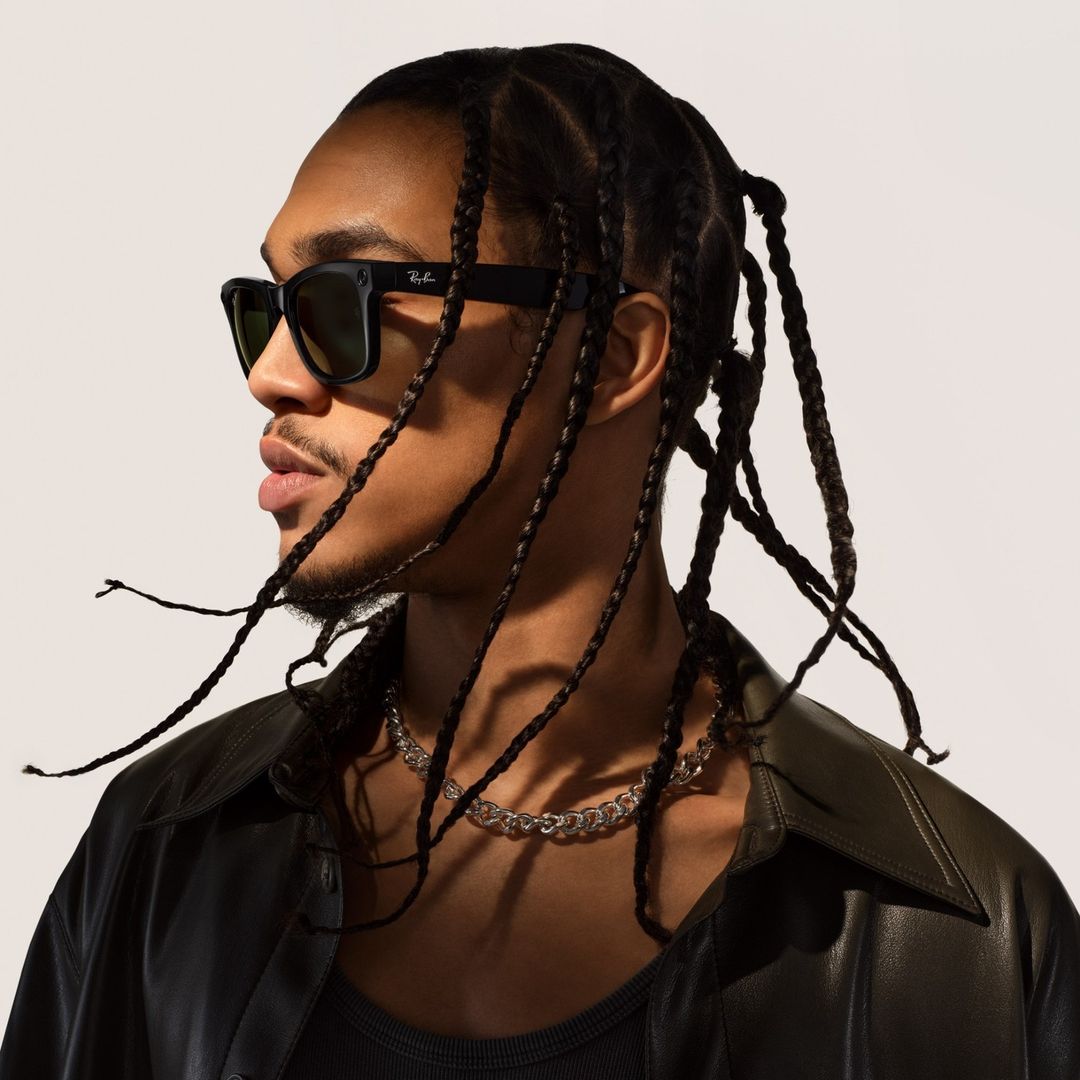 Profile portrait of a black man wearing black sunglasses and a dark leather shirt against a white seamless backdrop.