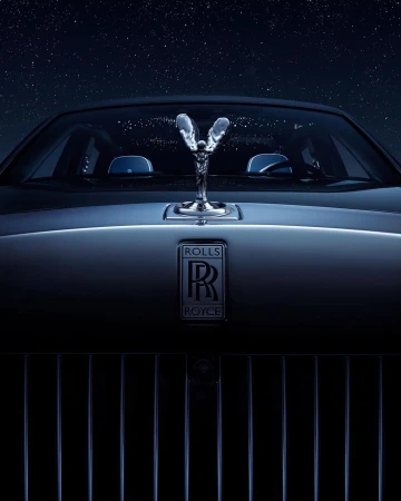 Silver Rolls Royce front view with the Spirit of Ecstasy hood ornament under a night sky filled with stars. Automotive elegance.