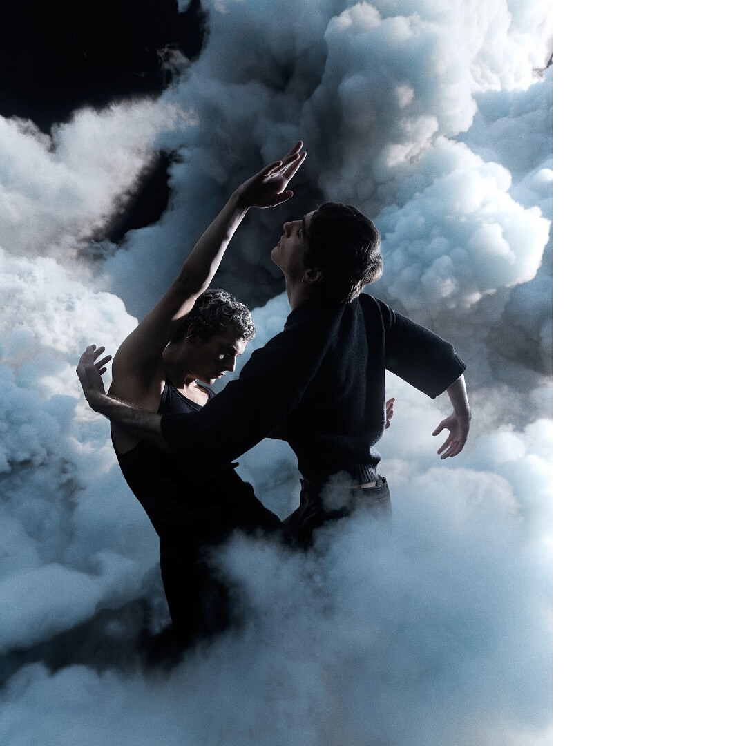 Dramatic studio shot of two dancers in black performing an artistic routine amidst smoky haze against a dark background, artistic expression.
