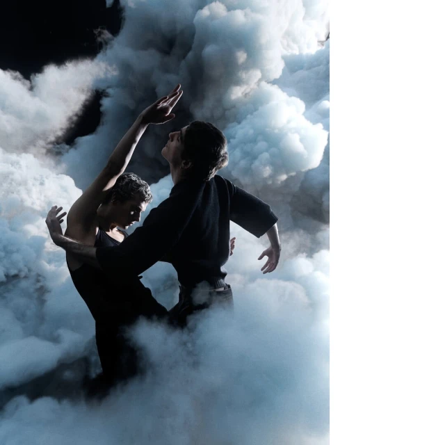 Dramatic studio shot of two dancers in black performing an artistic routine amidst smoky haze against a dark background, artistic expression.