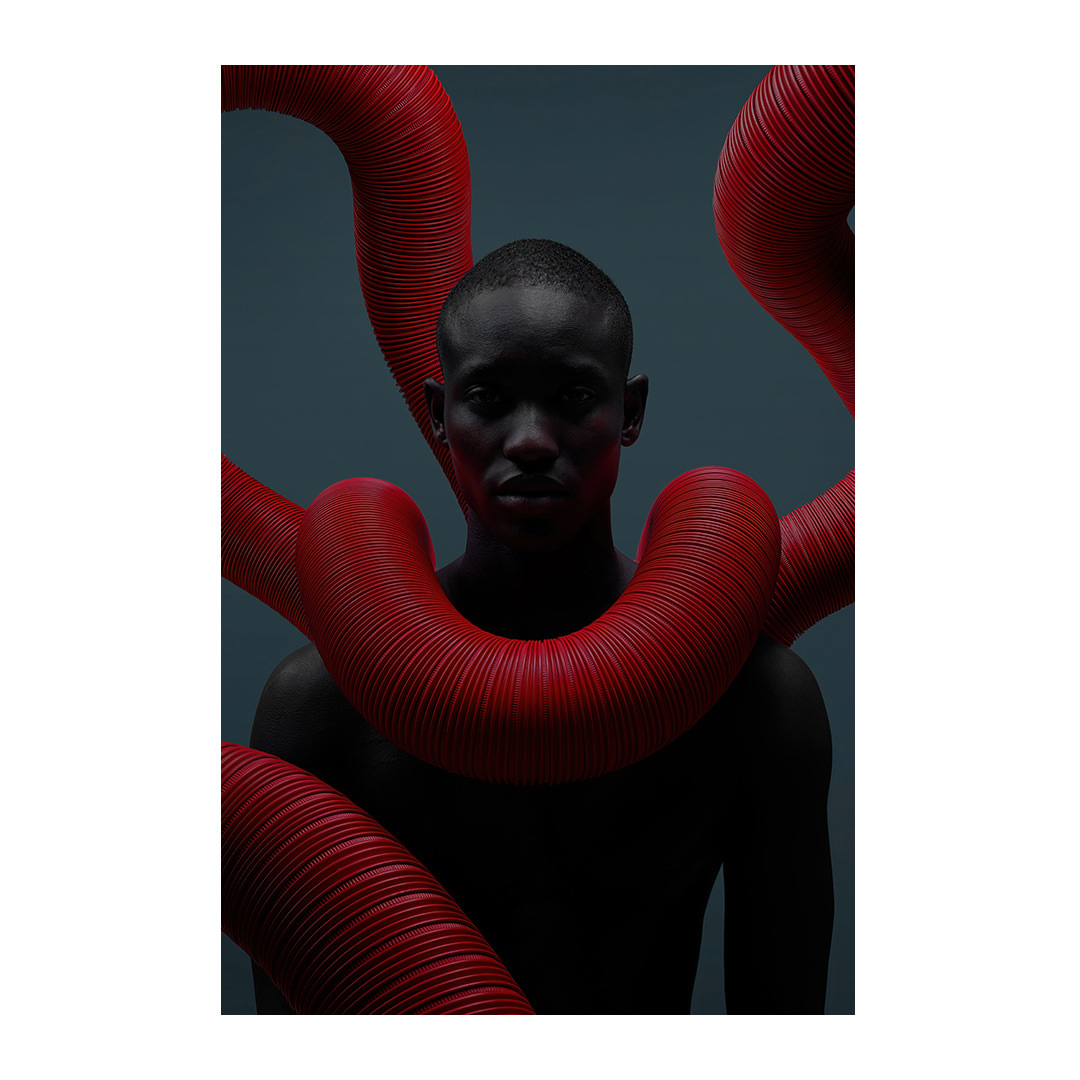 Portrait of a dark-skinned male surrounded by bright red corrugated flexible tubes on a dark grey backdrop in eye-level studio shot.