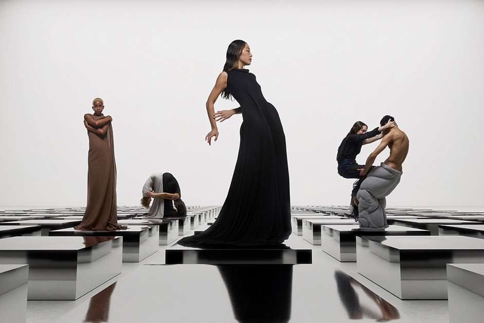 Fashion shot features women in gowns posing in a brightly lit studio with square podiums; one woman is carried by a man.