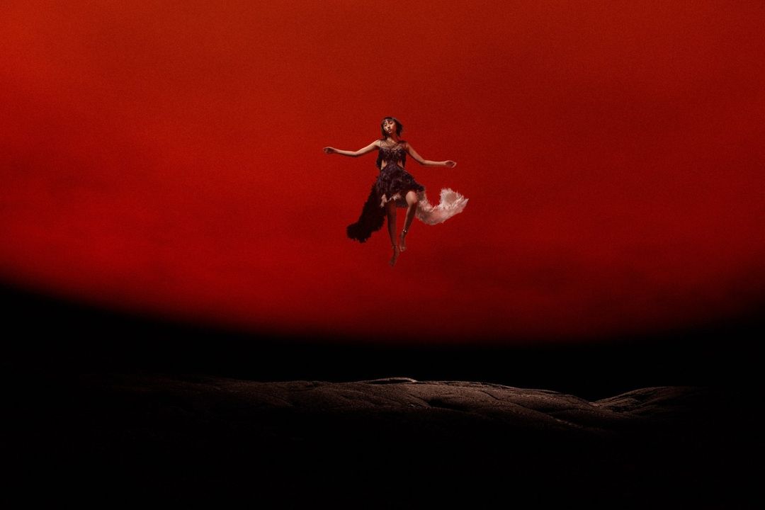 A woman in a black and white dress appears to be floating against a gradient red to black background, creating a surreal visual effect.