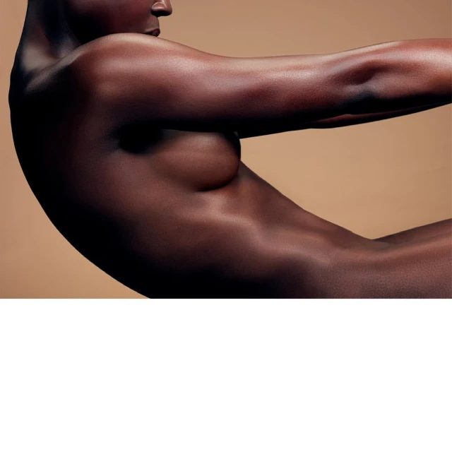Striking studio shot of a nude adult female with dark skin, posing against a tan backdrop, showcasing her body's curves and contours.