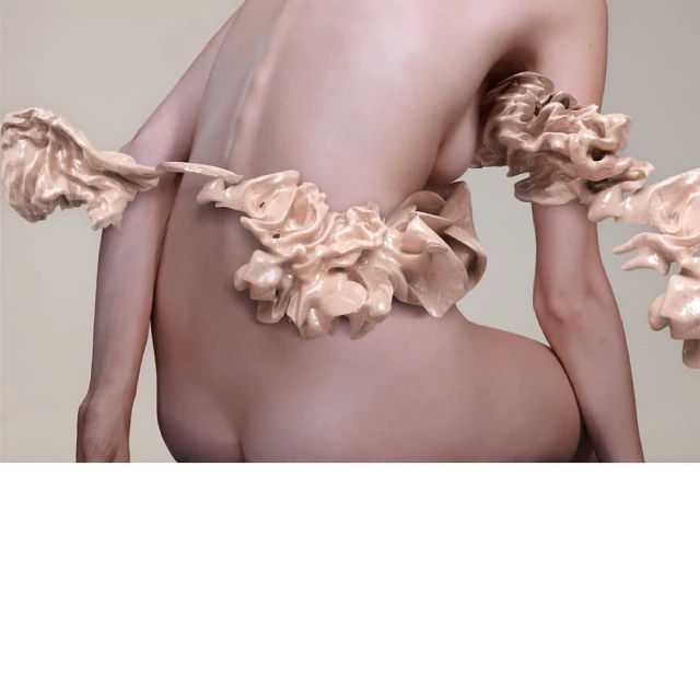 Back view of a nude adult female with fleshy pink ruffles. The pose is seated, in a studio with neutral background.