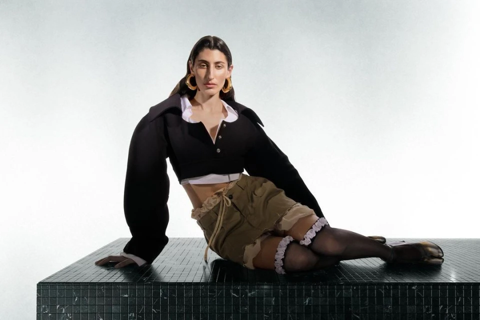 Woman in black crop top and khaki shorts sitting on a black marble surface in a studio setting with soft, diffused lighting.