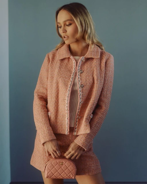 Elegant woman poses indoors wearing a tweed skirt suit, holding a quilted purse in a fashion photography studio with soft lighting.