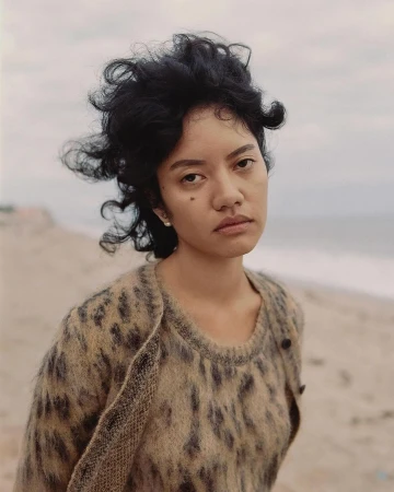Portrait of a woman with dark curly hair wearing a leopard print cardigan on a sandy beach