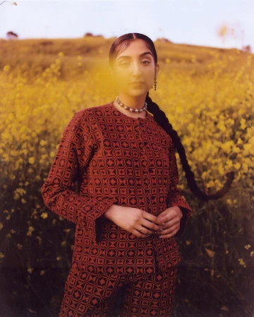 Woman wearing a patterned red and black long sleeve shirt standing outdoors in a field of yellow wildflowers
