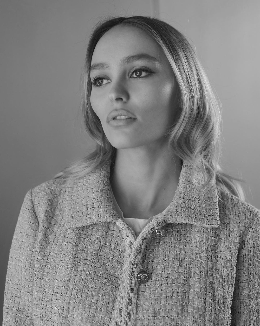 Black and white portrait of a young woman with wavy blonde hair wearing a tweed jacket and looking off-camera, with a neutral expression.