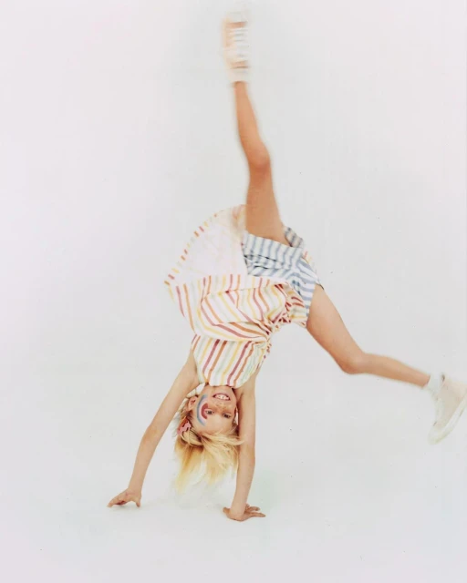 Young girl doing a cartwheel in a studio with a colorful striped dress and face paint, showcasing childhood and active lifestyle.