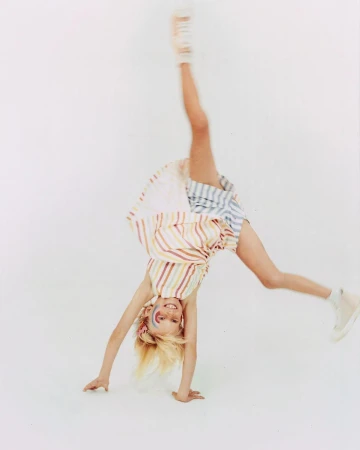 Young girl doing a cartwheel in a studio with a colorful striped dress and face paint, showcasing childhood and active lifestyle.