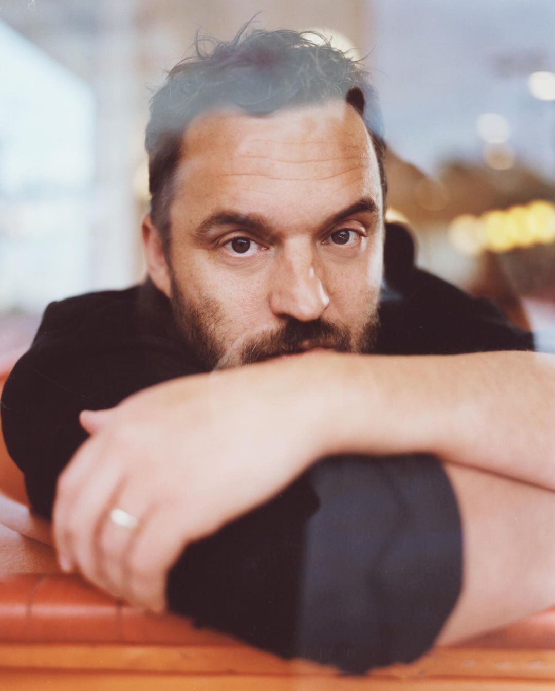 Indoor portrait of a middle-aged adult male with dark hair and a beard, resting his arms on a surface, wearing a black shirt.