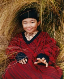 Child in red patterned sweater framed by tall dry grass photographed by Pat Martin