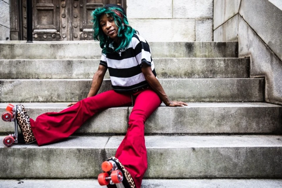 Person on roller skates sitting on concrete steps, wearing a striped shirt and bright red pants, showcasing urban street style.