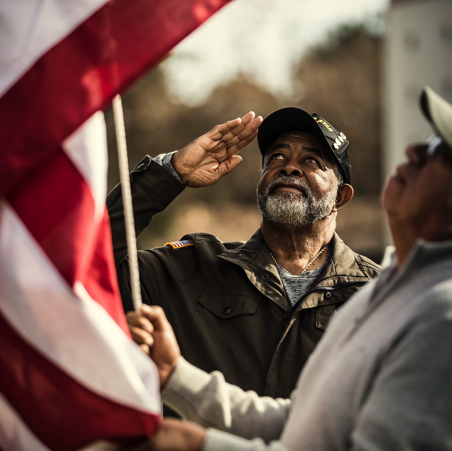 Two men salute a waving American flag outdoors in a patriotic display of respect and remembrance on a sunny day.