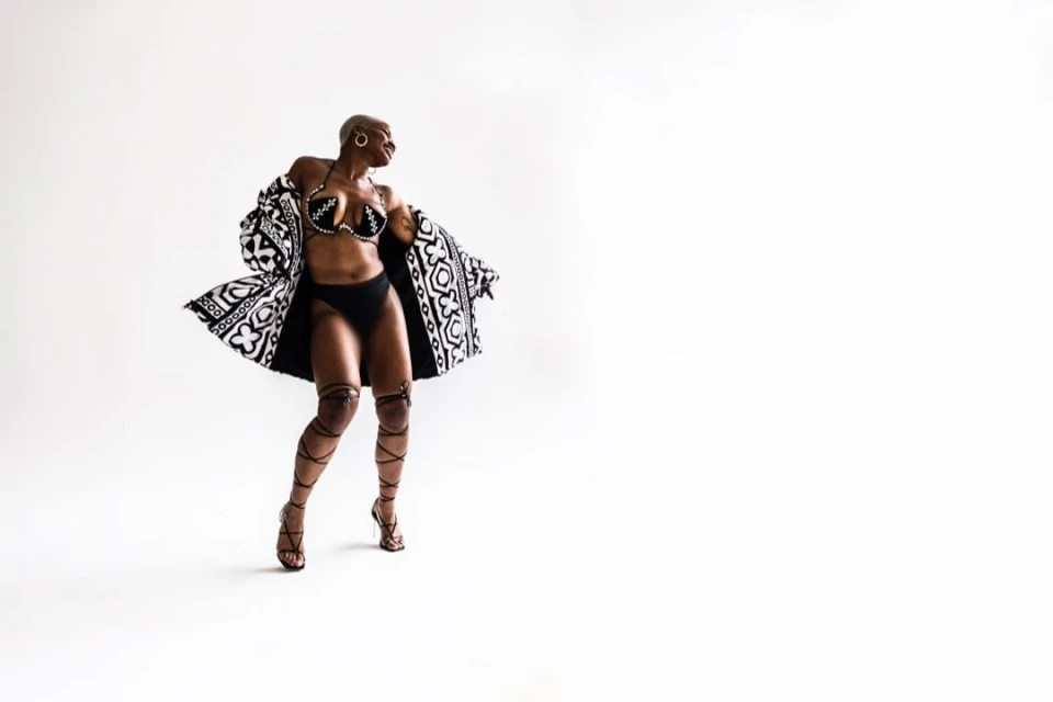 Adult female poses in a patterned bra and bottoms with matching coat in a studio setting, looking to the side with wind-blown coat.
